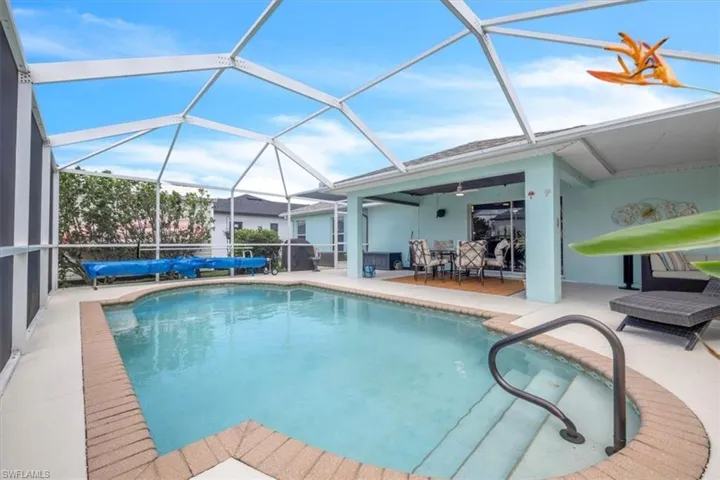 Screened enclosure featuring a swimming pool with a brick coping, an integrated pool handrail, and a covered patio area