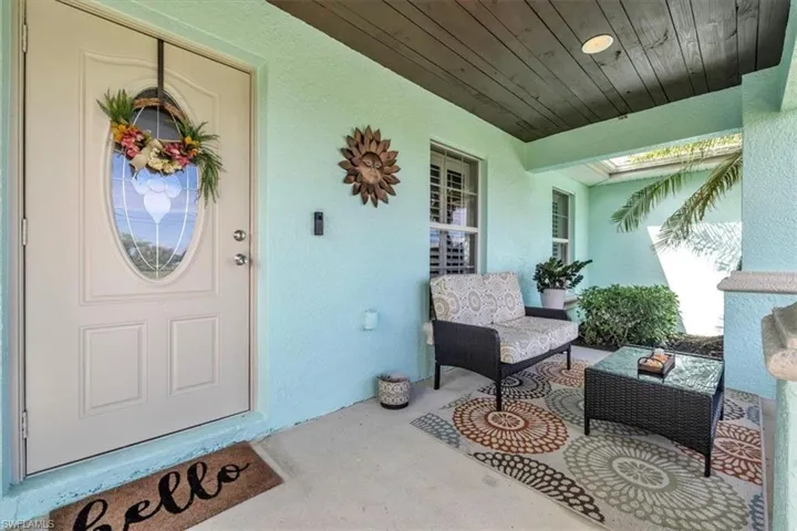 Covered front porch with wood-finish ceiling, decorative front door with oval glass insert, and stucco exterior