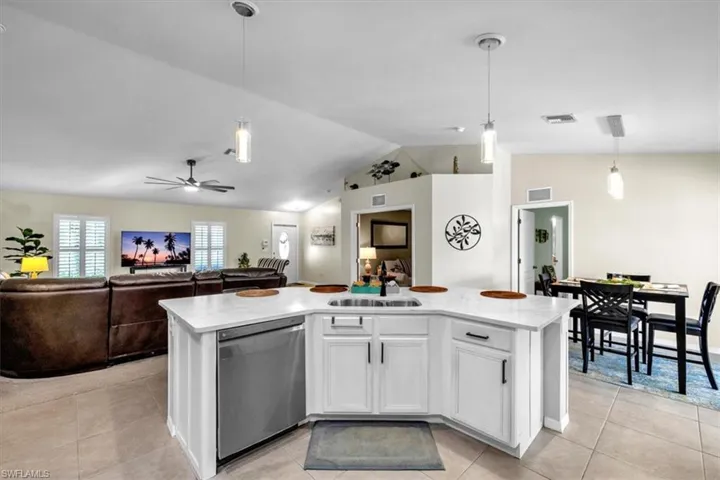 Open-concept kitchen with white cabinetry and a stainless steel dishwasher, featuring a dining area with pendant lighting, and tile flooring throughout