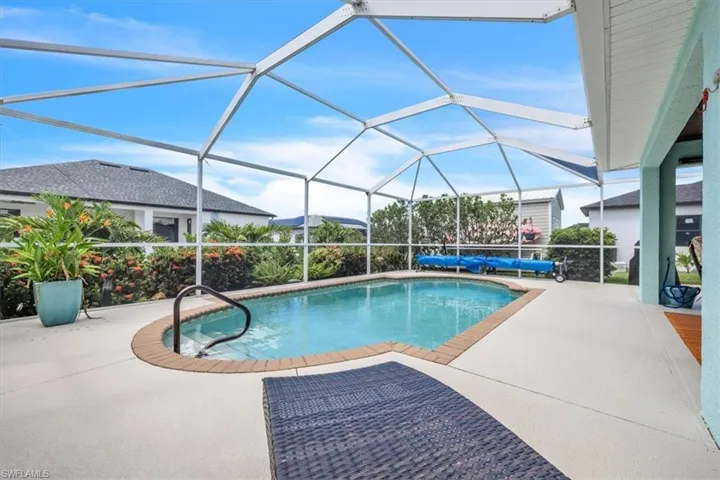 Screened pool enclosure featuring a light blue pool, brick-edged pool deck, and a contrasting light exterior wall