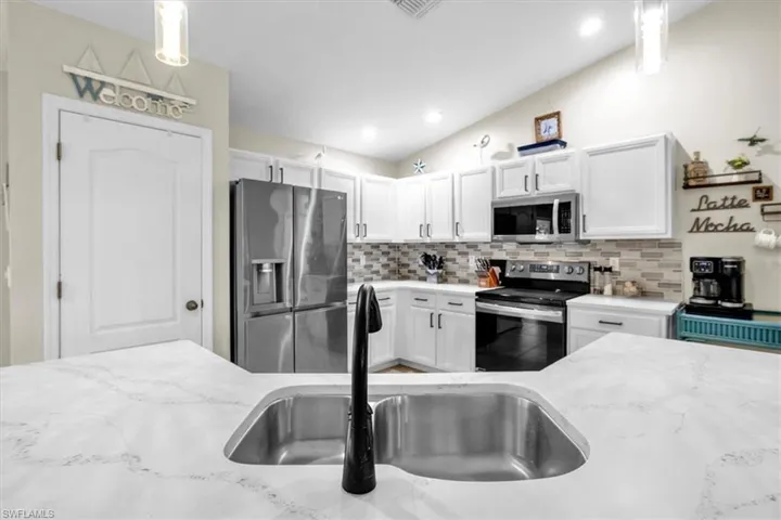 Kitchen featuring white cabinetry, stainless steel appliances, a tile backsplash, and a double basin sink with a matte black faucet