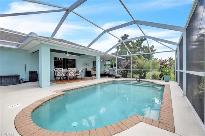 Screened-in pool deck featuring a swimming pool with brick coping, an attached covered patio, and a ceiling fan