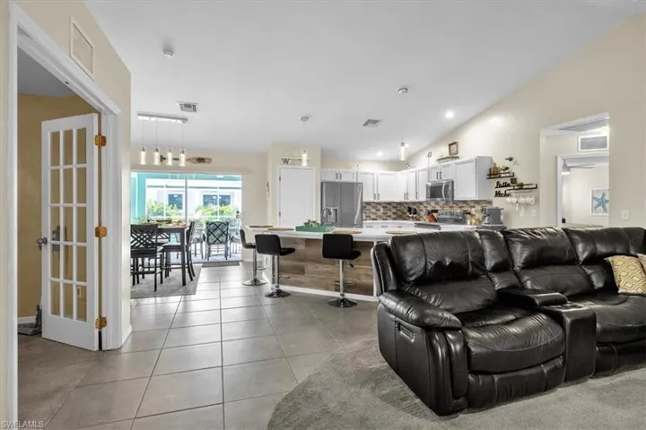 Open-concept living area featuring vaulted ceilings, tile flooring, and a kitchen with white cabinetry and an island with bar seating