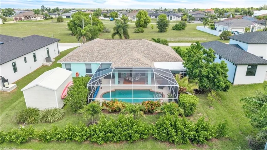 Screened-in pool with a paved deck, mature landscaping, and a detached storage shed