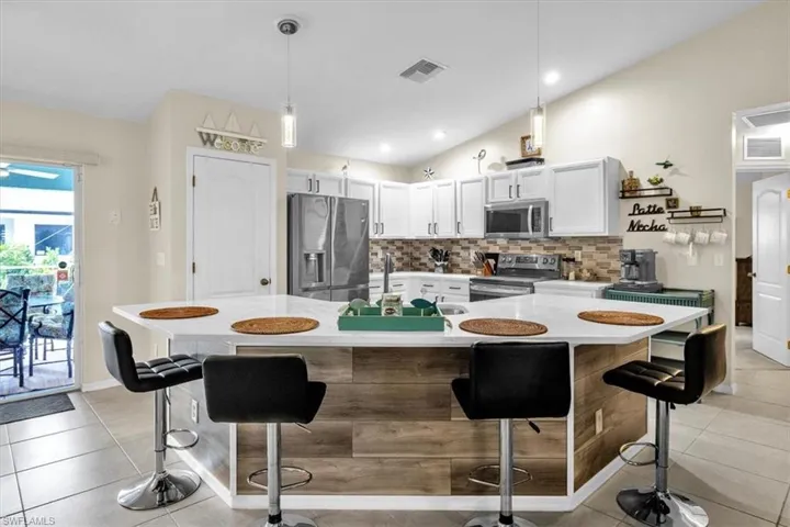 Kitchen featuring a large island with wood-finish paneling, white cabinetry, integrated stainless steel appliances, a tile backsplash, and recessed lighting