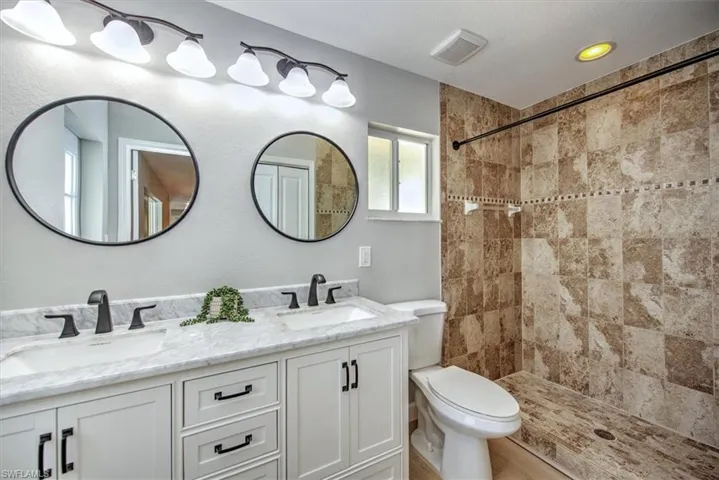 Full bath featuring a tile shower, visible vents, a sink, and toilet