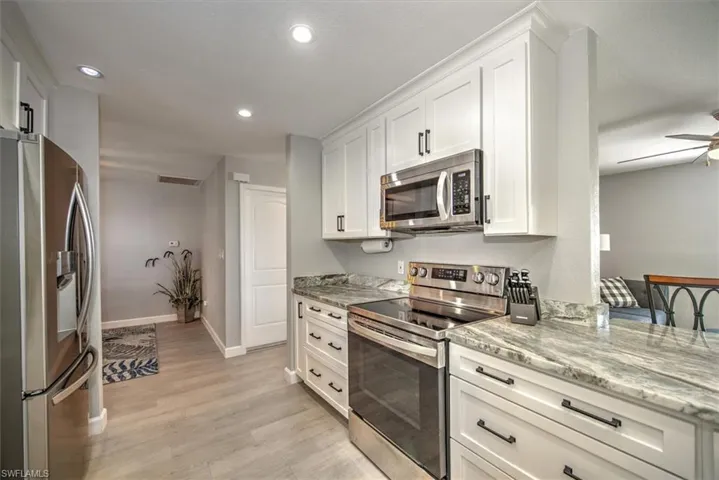 Kitchen featuring white cabinets, stainless steel appliances, light stone counters, and light wood finished floors