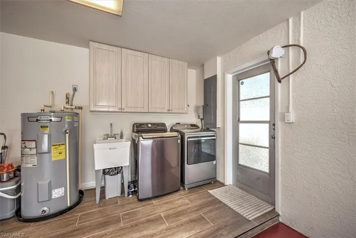 Washroom featuring water heater, wood tiled floor, cabinet space, washing machine and dryer, and electric panel