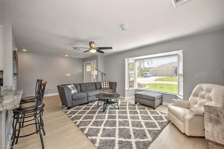 Living room with baseboards, visible vents, ceiling fan, and light wood-style flooring