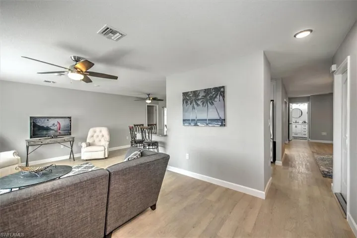 Living area featuring a textured ceiling, visible vents, baseboards, a ceiling fan, and light wood-type flooring