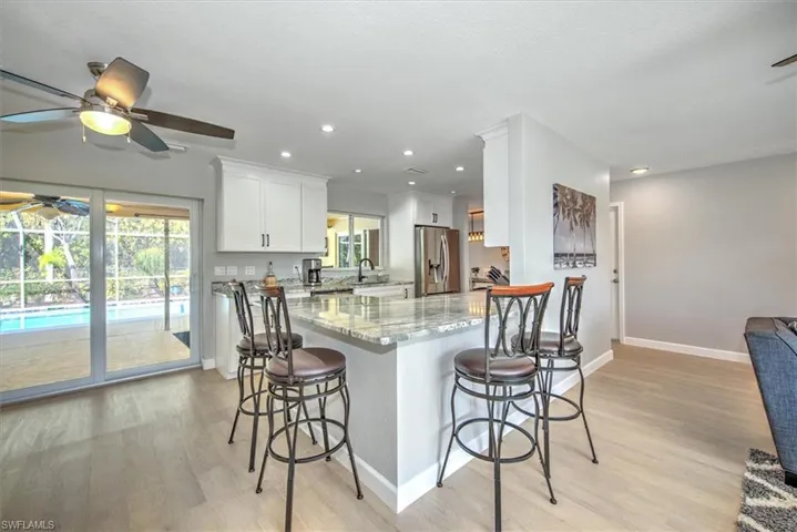 Kitchen featuring stainless steel fridge with ice dispenser, a breakfast bar area, light stone counters, and ceiling fan