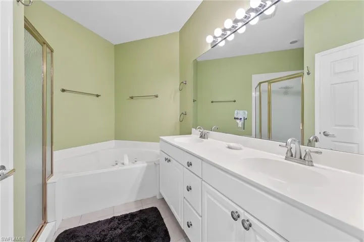 Full bath featuring a stall shower, light tile patterned flooring, double vanity, and a bath
