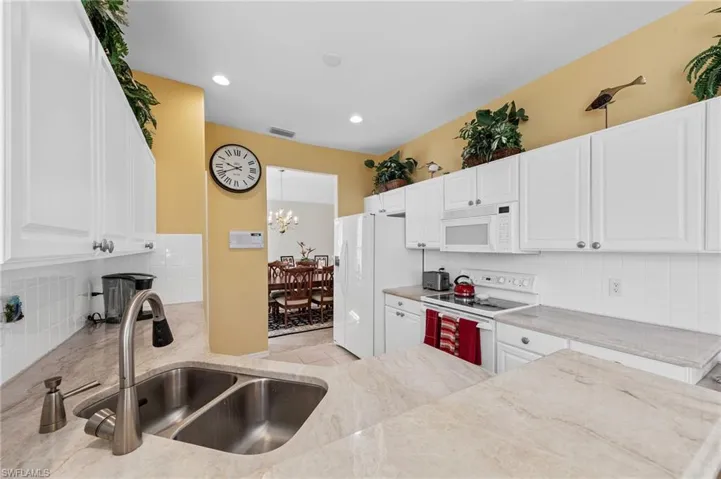 Kitchen with decorative backsplash, white appliances, white cabinets, recessed lighting, and decorative light fixtures