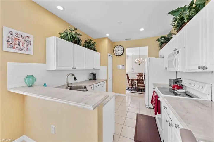 Kitchen with white appliances, tasteful backsplash, white cabinets, light tile patterned floors, and a peninsula