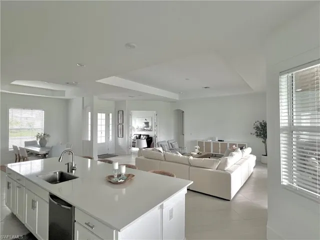 Kitchen with white cabinets, a center island with sink, a raised ceiling, light tile patterned flooring, and sink