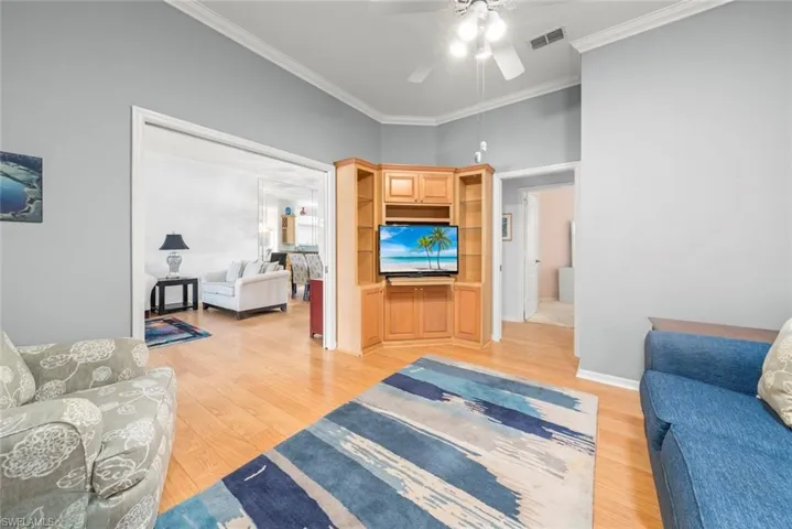 Living area with a ceiling fan, light wood-style flooring, and crown molding