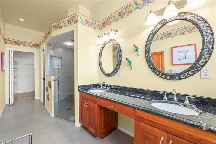 Bathroom featuring a shower stall, double vanity, a walk in closet, tile patterned floors, and baseboards