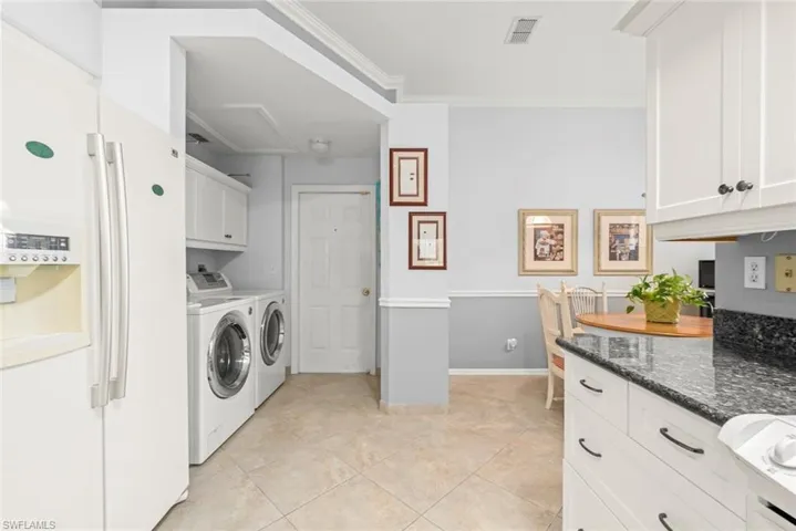 Washroom featuring washer and clothes dryer, crown molding, light tile patterned flooring, baseboards, and cabinet space