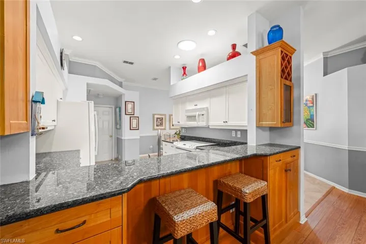 Kitchen featuring white appliances, dark stone counters, crown molding, light wood-type flooring, and white cabinetry