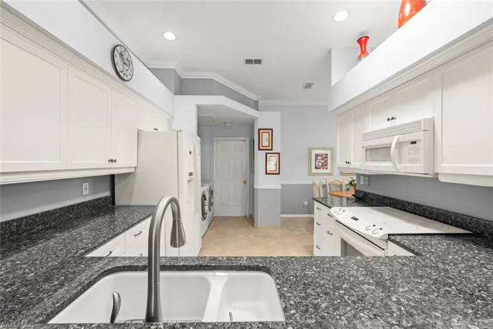 Kitchen with white appliances, a sink, crown molding, dark stone countertops, and white cabinetry