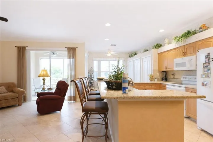 Kitchen with white appliances, a kitchen breakfast bar, light wood finish cabinetry, plenty of natural light, and ornamental molding