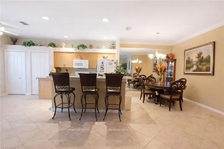 Kitchen featuring light wood finish cabinets, a kitchen island, white appliances, a breakfast bar area, and suspended lighting
