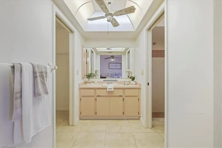 Full bath featuring ceiling fan, a tile shower, a skylight, double vanity, and tile patterned floors