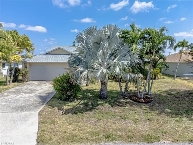 View of property hidden behind natural elements with a front yard, concrete driveway, and a garage