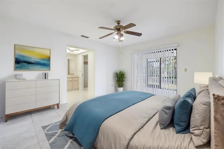 Bedroom with light tile patterned floors, ceiling fan, and ensuite bath