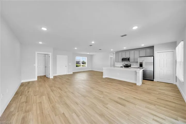 Open-concept living area featuring wood-finish flooring, a kitchen island with seating, grey cabinetry, stainless steel appliances, and recessed lighting