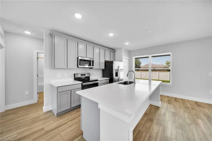 Kitchen featuring a central island with an undermount sink, light gray cabinetry, stainless steel appliances, and wood-finish flooring