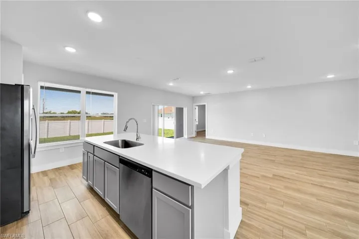 Open-concept living space featuring a kitchen island with an integrated sink, stainless steel dishwasher, and light-colored countertops