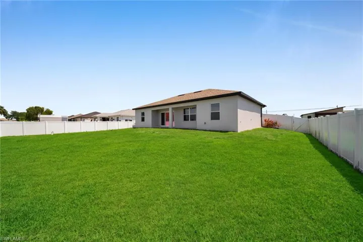 Expansive backyard featuring a lush lawn, white privacy fencing, and a light-colored stucco exterior with a brown shingle roof