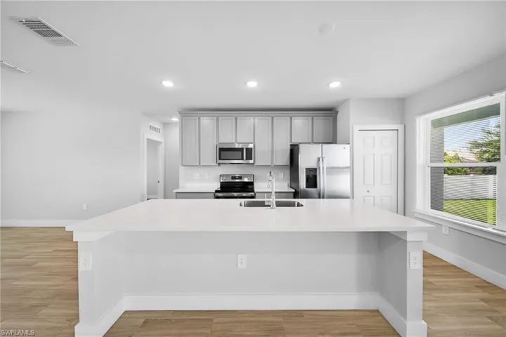 Kitchen with a large island featuring a double-basin sink, light-toned cabinetry, stainless steel appliances, and wood-finish flooring