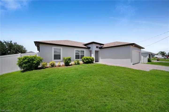 Contemporary stucco exterior featuring a brown shingle roof, integrated garage, front entry with recessed lighting, and a well-maintained lawn with landscaping
