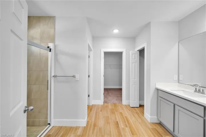 Bathroom featuring wood-finish flooring, a glass-enclosed shower with tiled walls, a vanity with a white countertop and gray cabinetry, and a framed mirror