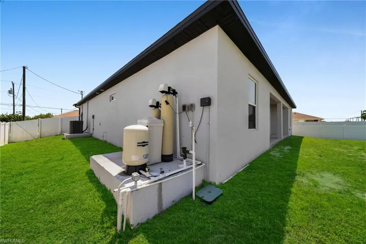 Manicured lawn with a stucco exterior, featuring a water filtration system, central air conditioning unit, and covered patio area