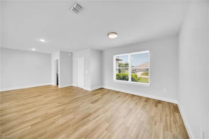 Spacious room featuring wood-finish tile flooring, recessed ceiling lighting, a flush-mount ceiling light fixture, and a large window with white trim