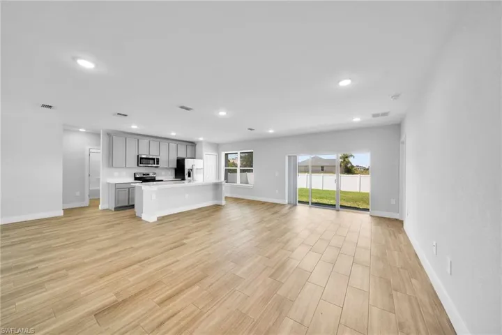 Open-concept living space featuring wood-finish flooring throughout, a kitchen island with a breakfast bar, recessed lighting, and sliding glass doors to the exterior