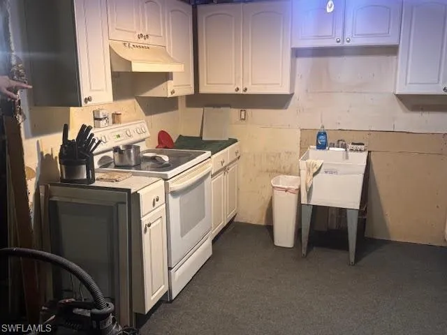 Kitchen featuring white electric range, under cabinet range hood, light countertops, and dark carpet