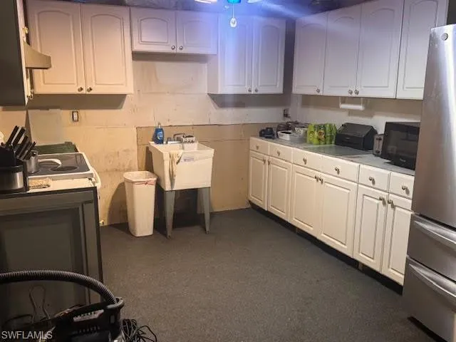 Kitchen featuring freestanding refrigerator, light countertops, white cabinetry, and black microwave