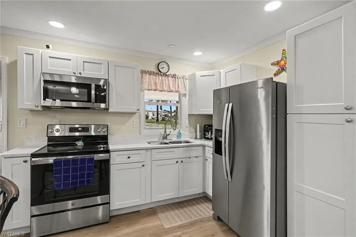 Bright kitchen featuring stainless steel appliances, white shaker-style cabinetry, light countertops, a double basin sink, and recessed lighting