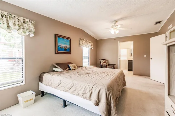 Bedroom featuring connected bathroom, ceiling fan, light colored carpet, a textured ceiling, and lofted ceiling
