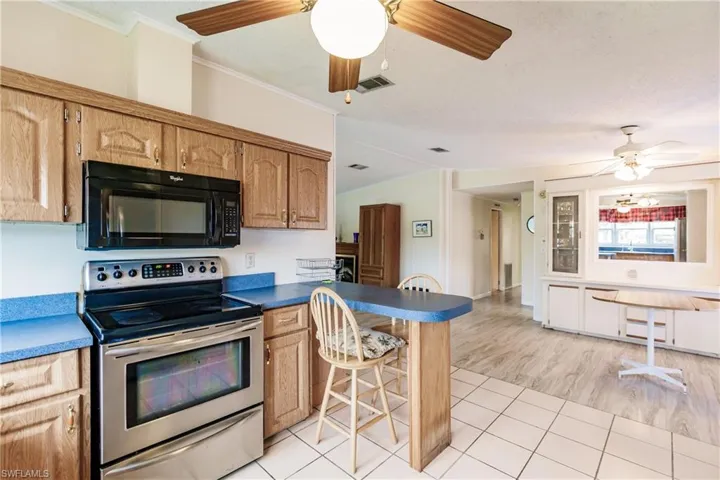 Kitchen featuring kitchen peninsula, light hardwood / wood-style floors, stainless steel electric stove, ceiling fan, and ornamental molding