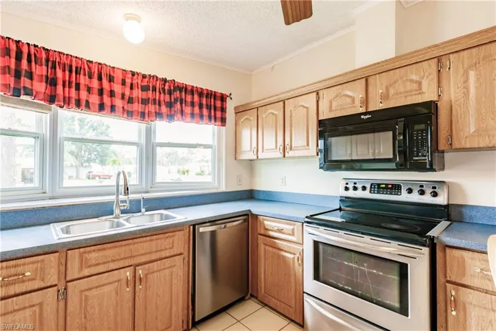 Kitchen with stainless steel appliances, crown molding, sink, a textured ceiling, and light tile patterned floors