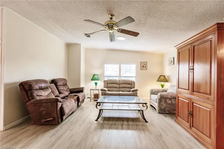 Living room with a textured ceiling, ceiling fan, and light wood-type flooring