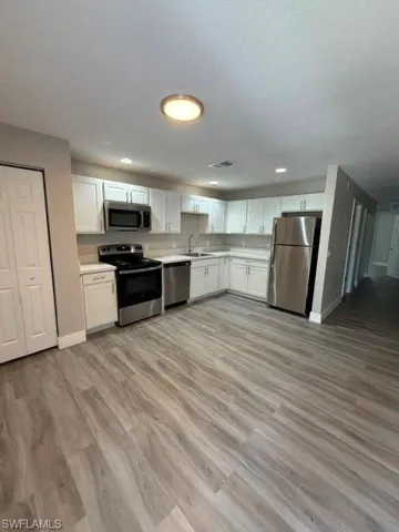 Open-concept kitchen featuring white shaker cabinetry, light-toned countertops, and stainless steel appliances
