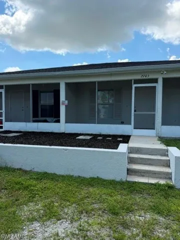 Screened porch entry with concrete steps and a raised garden bed with stepping stones