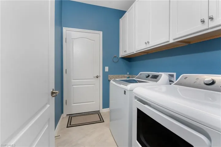 Clothes washing area featuring baseboards, washing machine and dryer, cabinet space, and light tile patterned flooring