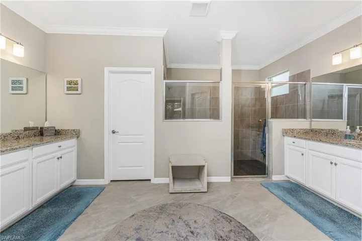 Full bath featuring crown molding, baseboards, two vanities, and a stall shower